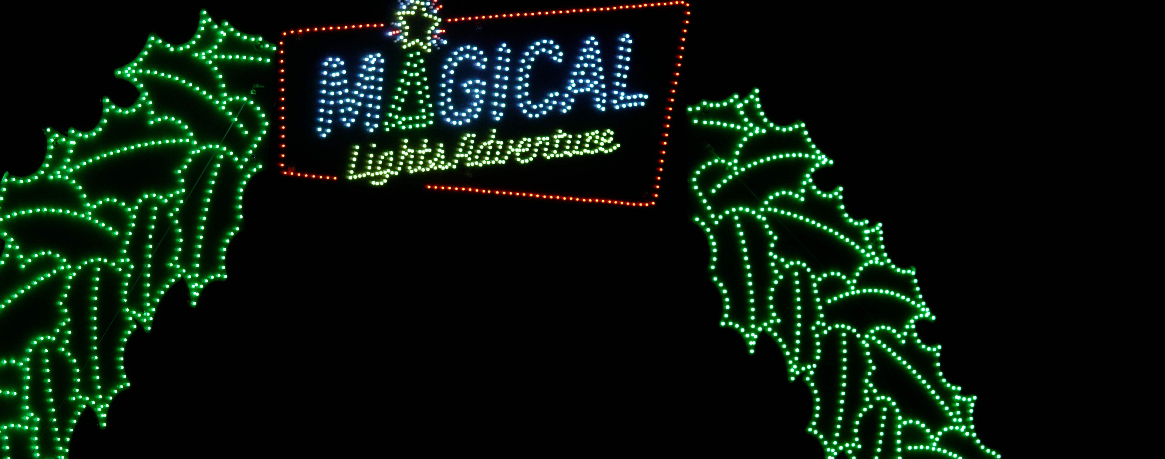 Illuminated green holly archway with the Magical Lights Adventure neon sign at the entrance