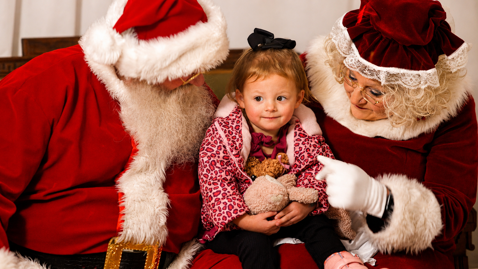 Santa and Mrs. Claus smiling with a young child holding a plush toy